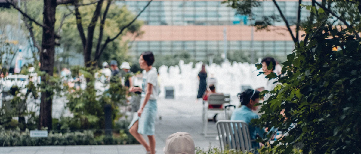 Praça arborizada com uma fonte ao fundo e pessoas circulando em uma manhã clara